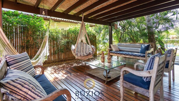 A covered outdoor seating area with a hammock, cushioned seating, and a glass table.