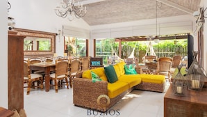 A spacious indoor area with a large wicker sofa, dining table, and chairs.