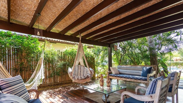 A covered outdoor seating area with a hammock, cushioned seating, and a glass table. - Bz37 Casa com Piscina a 200M da praia (Buzios)