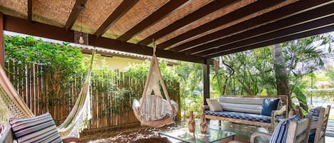 Un espace extérieur abrité avec des sièges confortables, un hamac et une table en verre.