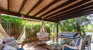 A covered outdoor seating area with a hammock, cushioned seating, and a glass table. - Bz37 Casa com Piscina a 200M da praia (Buzios)