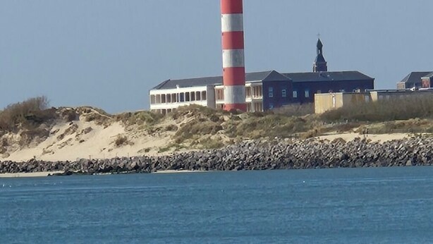 Een gebouw aan de kust met een vuurtoren, een zandstrand en een rotsachtige kustlijn.