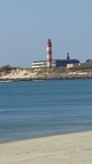 A coastal building with a lighthouse, a sandy beach, and a rocky shoreline.