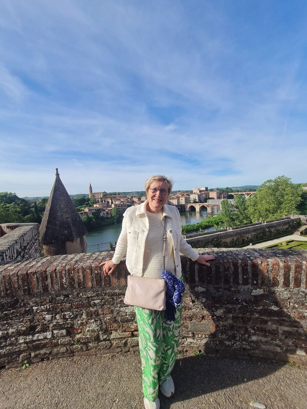 A person standing on a stone bridge with a cityscape in the background.