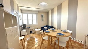 Een eetgedeelte met een ronde houten tafel, witte stoelen en een blauwe bank op de achtergrond.