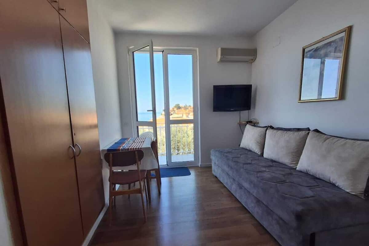 A room with a sofa, a table with chairs, a TV, and a sliding glass door leading to a balcony.