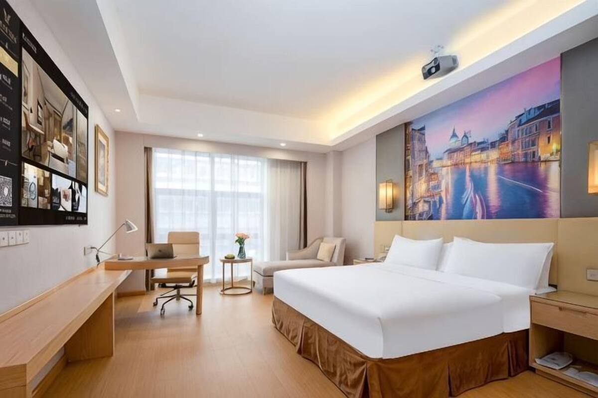 A hotel room with a bed, desk, chair, and a large window.