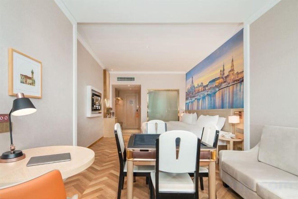 A hotel room with a dining area, a sofa, and a painting of a cityscape.