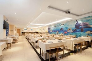 A restaurant with tables set for dining, a mural of marine life on the wall, and a ceiling with recessed lighting. - Vienna International Hotel Zhanjiang North Railway Station Dingsheng Plaza (Zhanjiang)