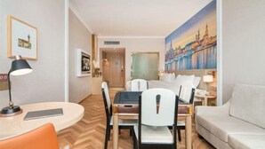 A hotel room with a dining area, a sofa, a painting of a cityscape, and a bed. - Vienna International Hotel Zhanjiang North Railway Station Dingsheng Plaza (Zhanjiang)
