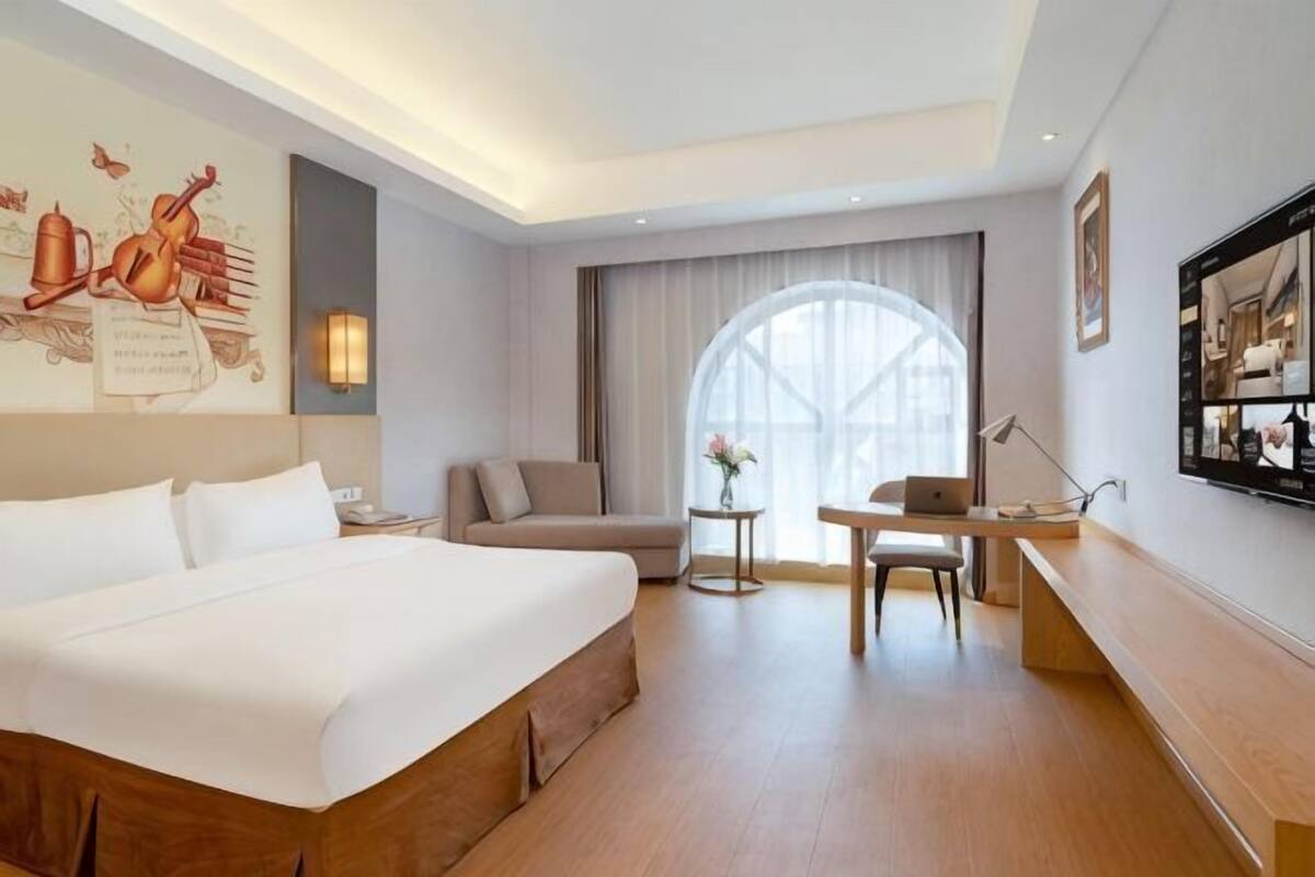 A hotel room with a large bed, a sofa, a small table, and a desk.