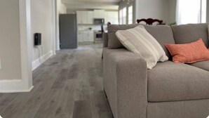 En moderne stue med en grå sofa, en lysekrone og udsigt til et køkken.