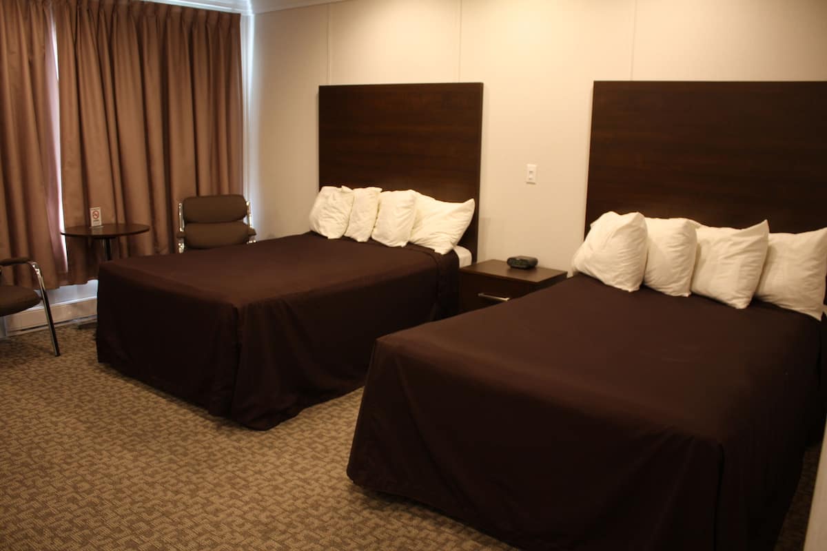 A hotel room with two beds, a chair, a small table, and a curtain.