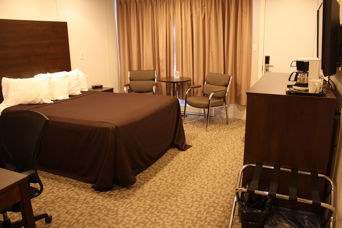 A hotel room with a large bed, two armchairs, a small table with a coffee maker, and a desk.
