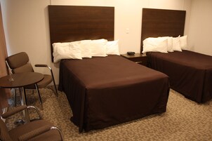 Habitación de hotel con dos camas, una mesita y dos sillas.
