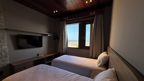 A hotel room with two beds, a TV mounted on the wall, and a window with a view of the beach. - VILLA PRIME BEACH (ARACAJU)