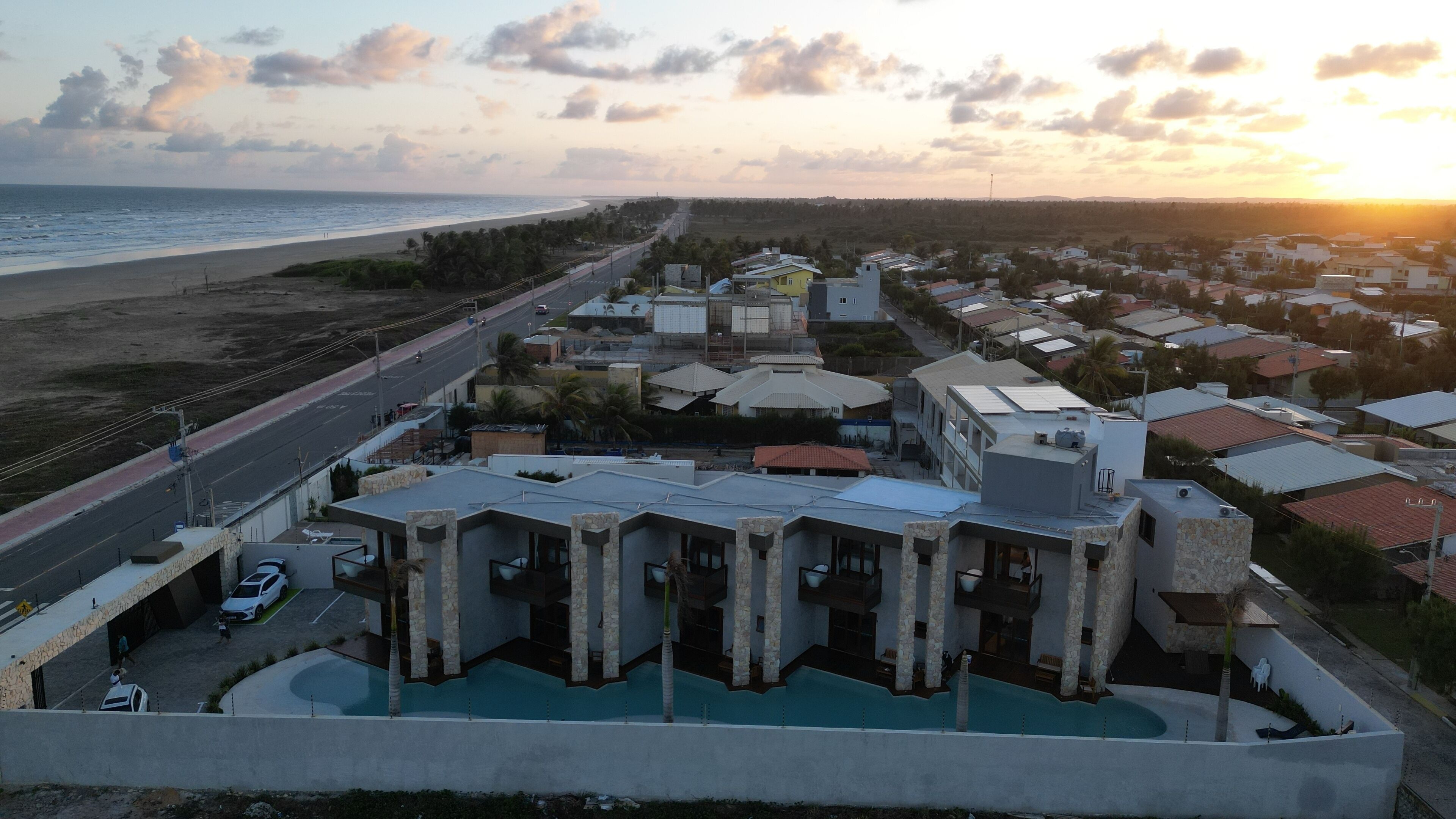 A modern building with a pool, located near a beach and a road.