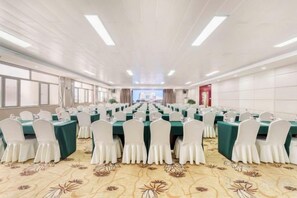 Un salón de conferencias con filas de mesas y sillas, una alfombra estampada y vistas por las ventanas.