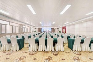 Un salón de conferencias con filas de mesas y sillas, una alfombra estampada y vistas por las ventanas.