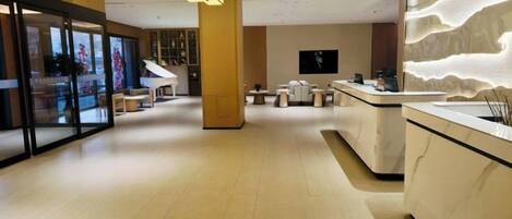 A modern hotel lobby with a reception desk, seating area, and a piano.