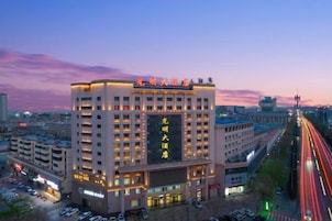 Un hotel de varios pisos con un letrero llamativo, rodeado de otros edificios y una calle concurrida con estelas de luz.