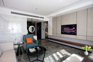 A modern hotel lobby with a sofa, a coffee table, a TV mounted on the wall, and a circular mirror. - Guangming Hotel (Jiuquan)