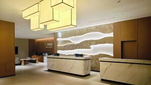 A hotel reception area with marble counters, a modern light fixture, and a textured wall design. - Guangming Hotel (Jiuquan)