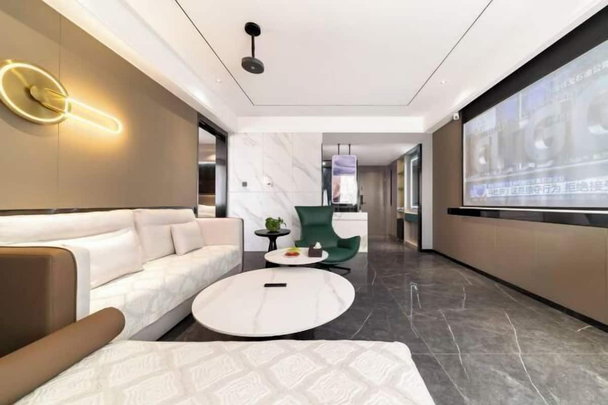 A modern hotel lobby with a sofa, a round coffee table, a green chair, and a large screen displaying text.