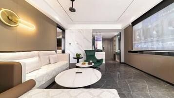 Eine moderne Hotelhalle mit einer Couch, einem runden Couchtisch, einem grünen Sessel und einem großen Bildschirm, der Text anzeigt.