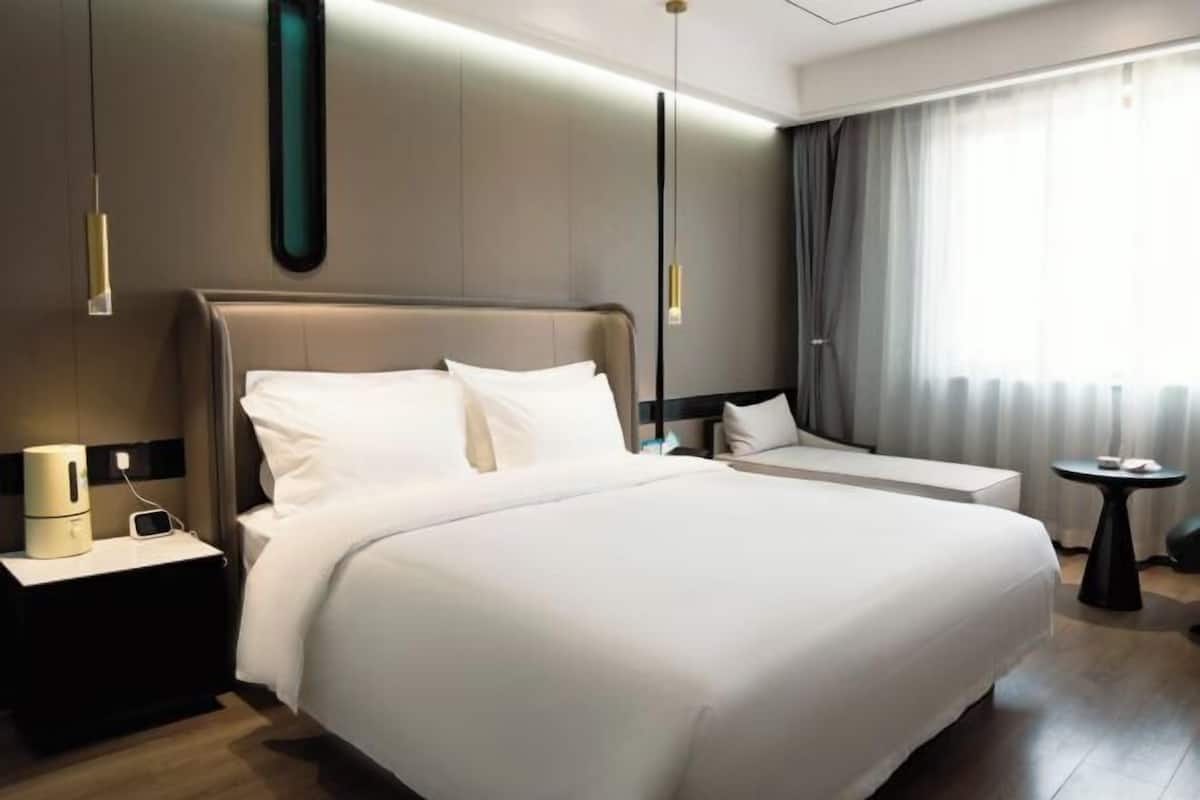 A modern hotel room with a large bed, bedside tables, a small seating area, and a view of the outdoors.