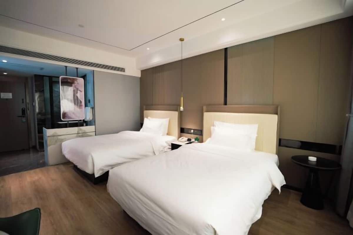 A hotel room with two beds, a small table, a chair, and a mirror.