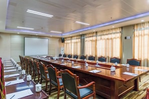 A conference room with a long table, chairs, and a projector screen. - Guangming Hotel (Jiuquan)