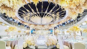 A banquet hall with round tables, white chairs, and floral decorations. - Guangming Hotel (Jiuquan)
