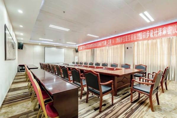 A conference room with a long table and chairs, a projector screen, and a banner. - Guangming Hotel (Jiuquan)