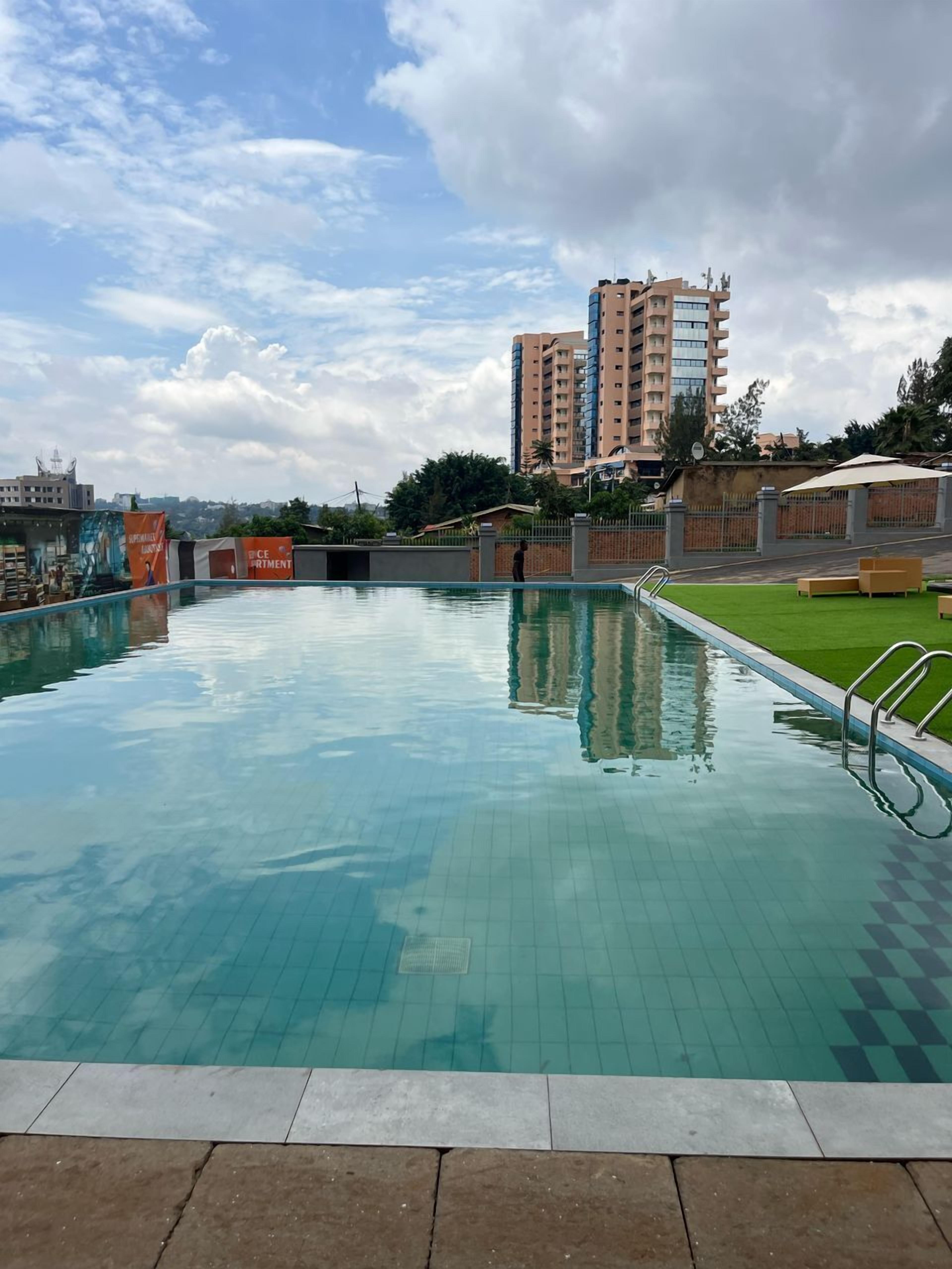 Ein Schwimmbecken mit gefliesten Rändern, eine Rasenfläche und ein hohes Gebäude im Hintergrund.