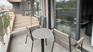 A modern balcony with a round table and chairs, a glass door leading to a dining area, and a view of the cityscape. - Kigali Greenland Serviced Apartments (Kigali)