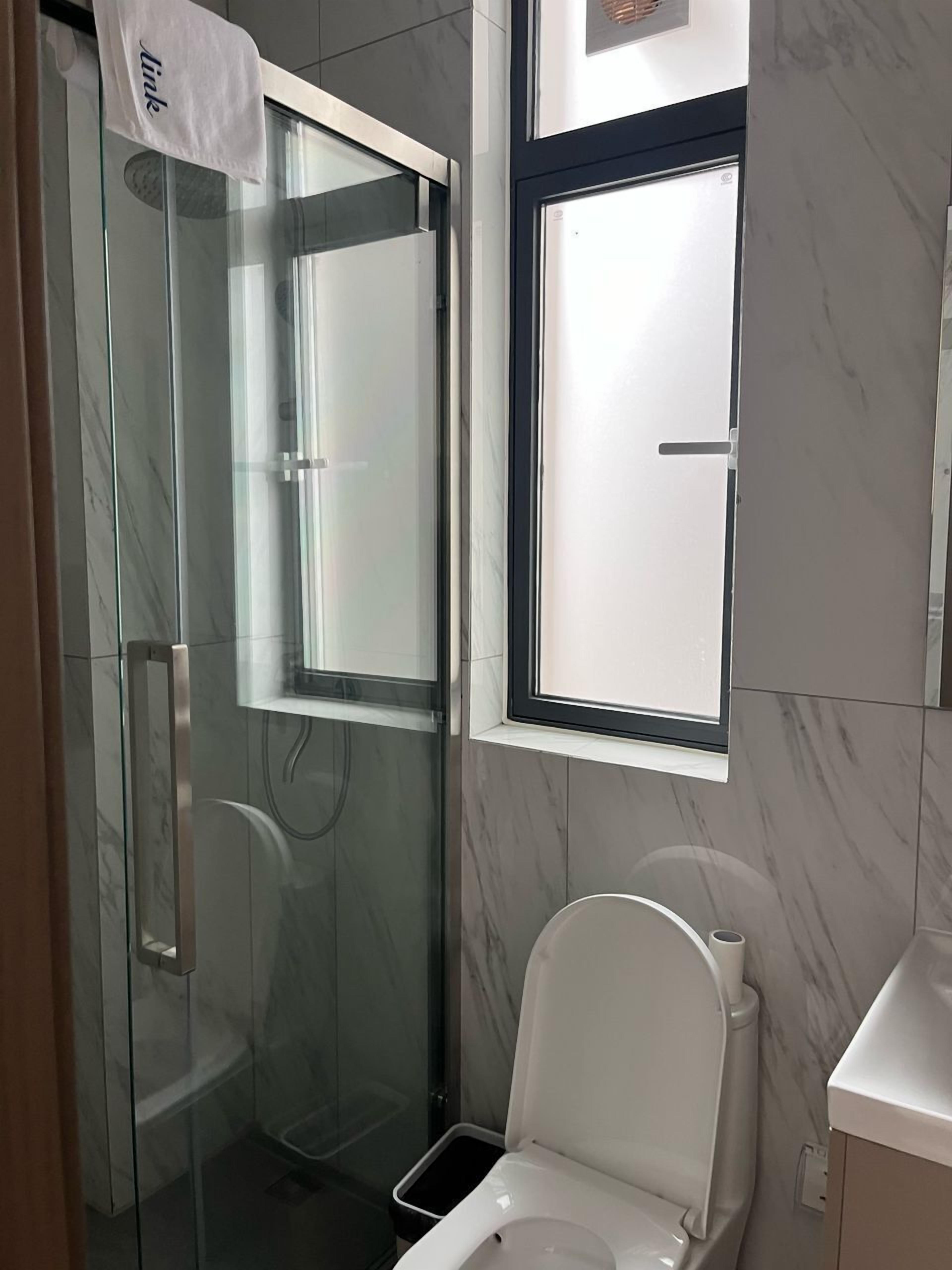 Une salle de bain moderne avec une douche à parois de verre, des toilettes et une fenêtre.