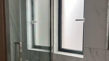 Une salle de bain moderne avec une douche à parois de verre, des toilettes et une fenêtre.