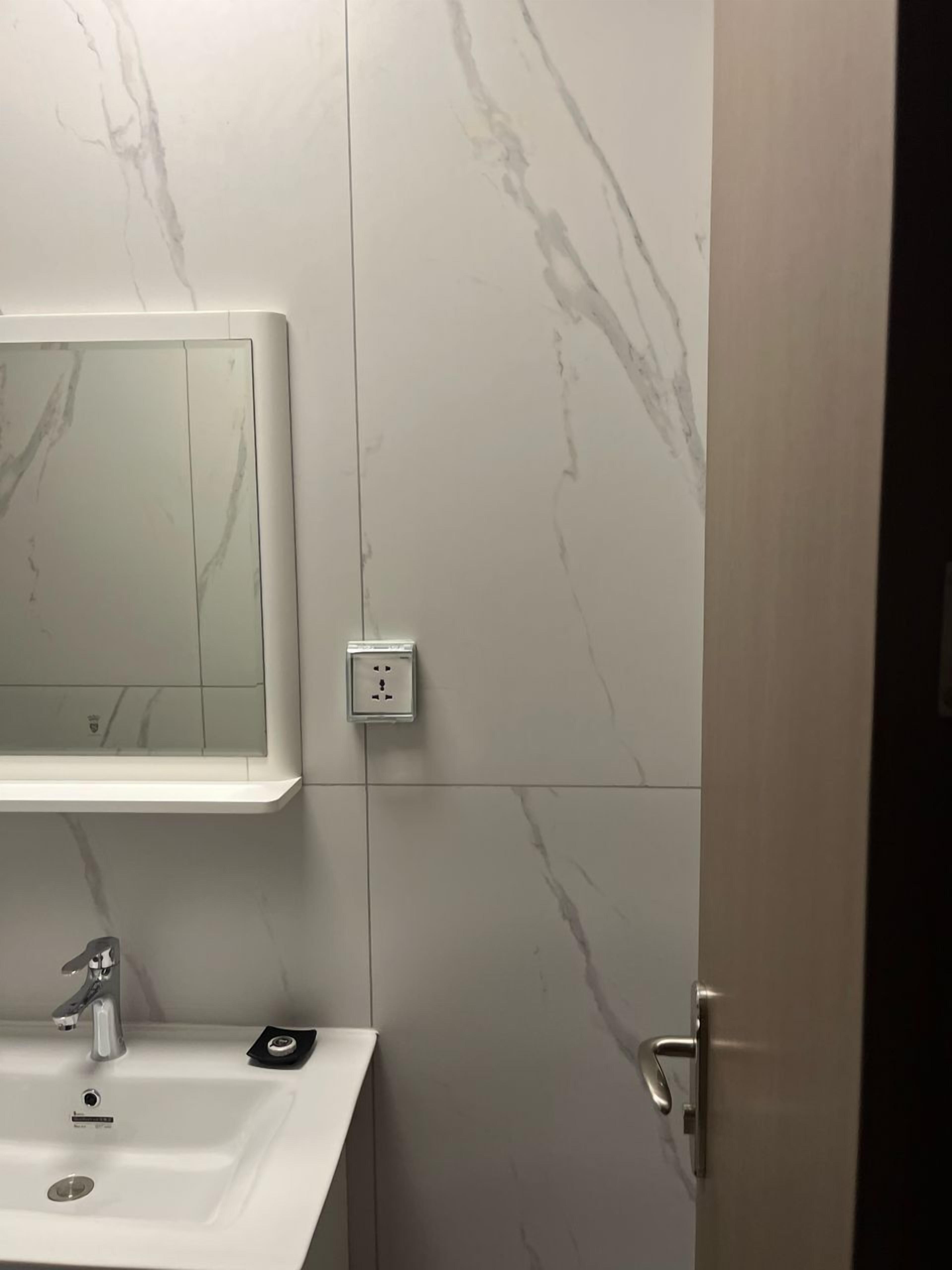 Een badkamer met een witte wastafel, een spiegel en een wand met marmerlook.