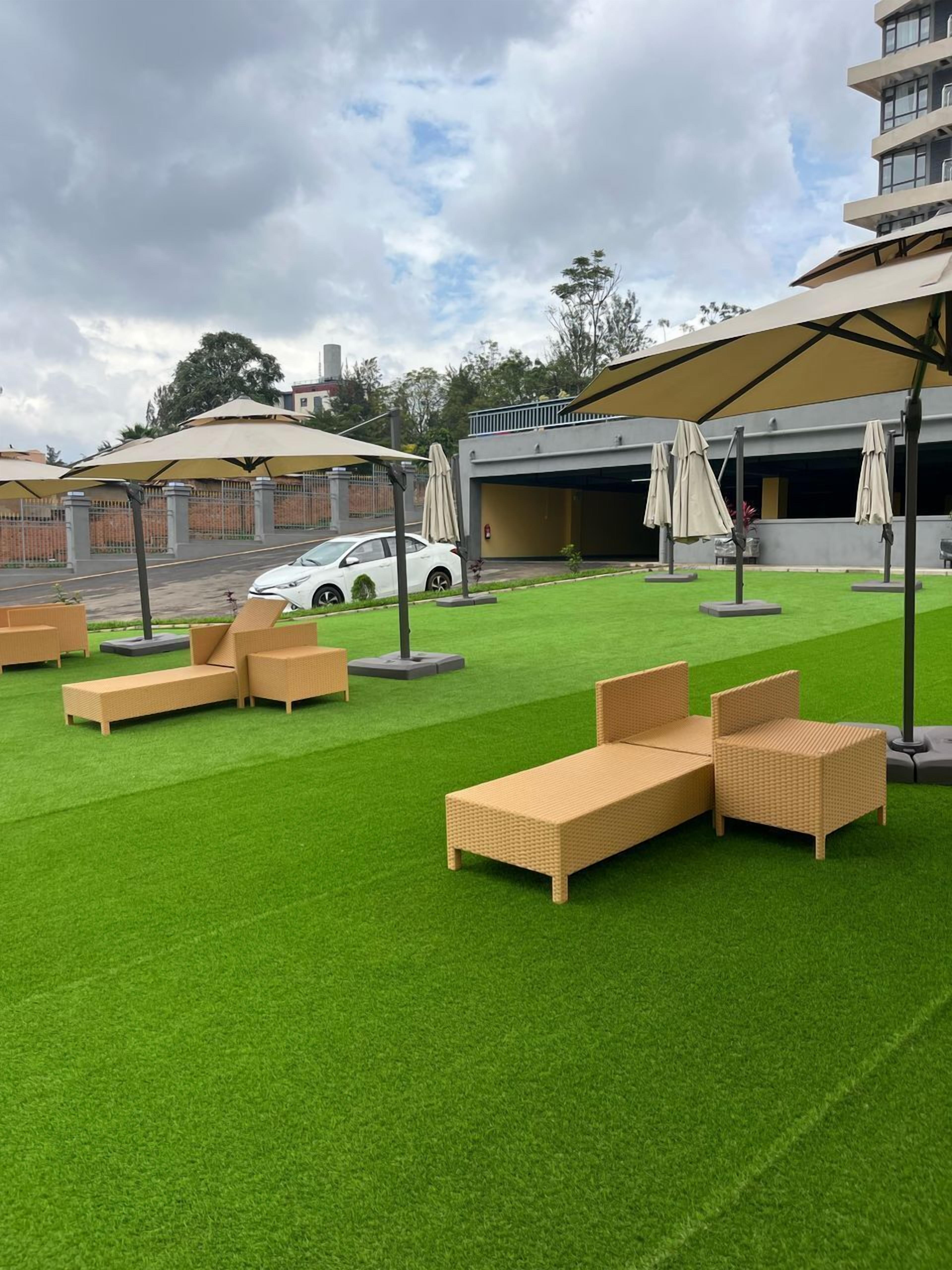 A rooftop lounge area with artificial grass, outdoor furniture, and umbrellas.