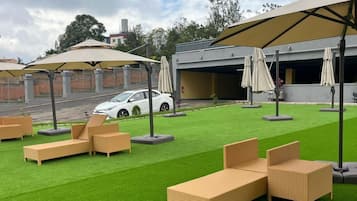A rooftop lounge area with artificial grass, outdoor furniture, and umbrellas.