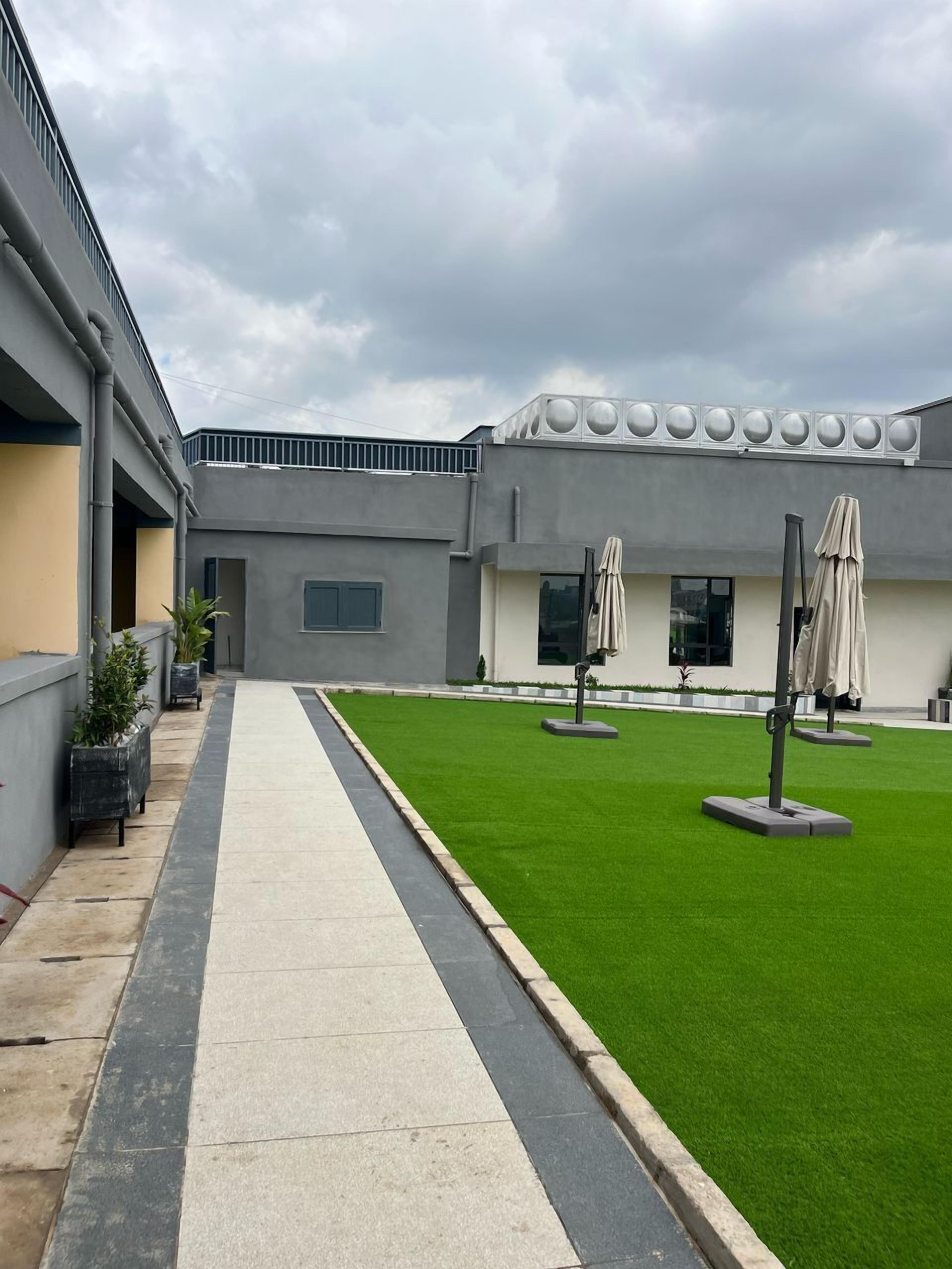 A courtyard with a paved walkway, green artificial grass, and outdoor umbrellas.