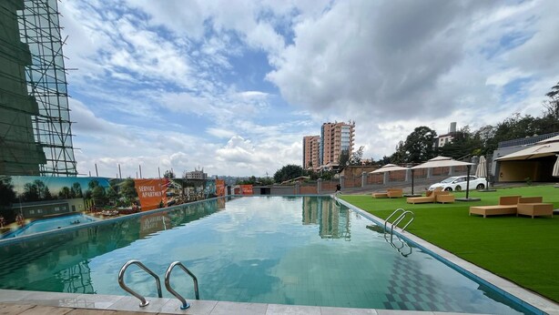 A swimming pool with a checkered pattern, surrounded by a grassy area and lounge chairs. - Kigali Greenland Serviced Apartments (Kigali)