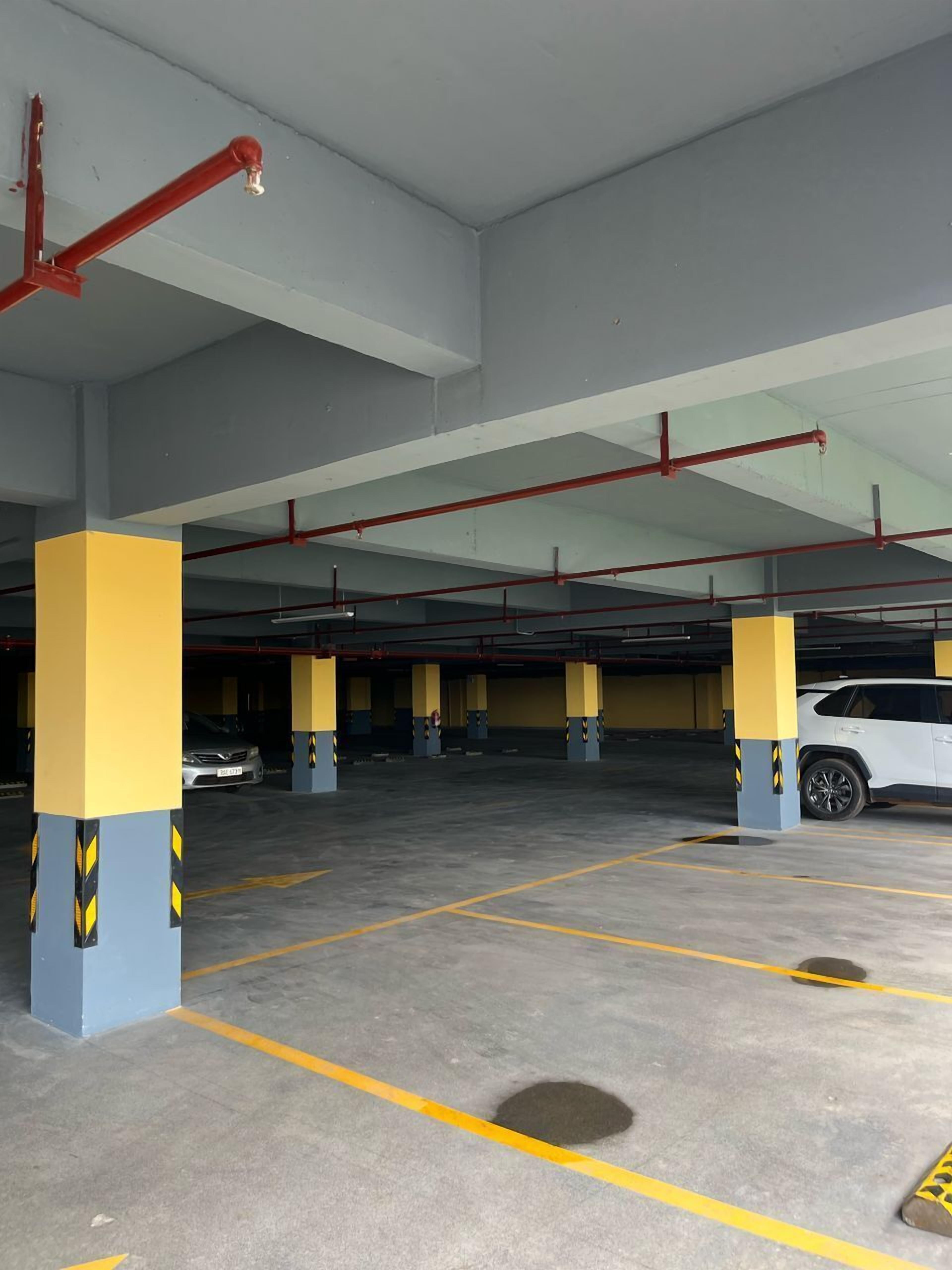 Un estacionamiento subterráneo con varios niveles, pilares amarillos y azules, y equipos de seguridad contra incendios rojos.
