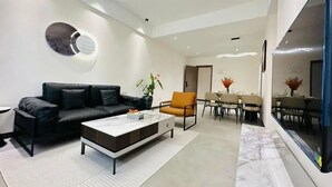 A modern living room with a black leather sofa, a white coffee table, and a dining area with a table and chairs. - Kigali Greenland Serviced Apartments (Kigali)