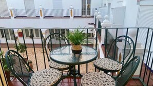 Eine kleine Terrasse im Freien mit einem runden Glastisch und vier Stühlen, umgeben von einem Metallzaun.