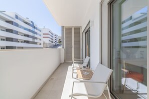 Een balkon met witte stoelen en een tafel, met uitzicht op een stadsgezicht met moderne gebouwen.