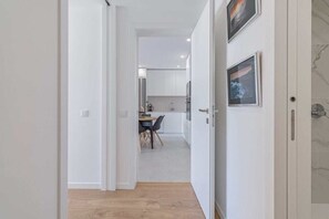 A corridor leading to a modern kitchen with white cabinetry and a dining area with a table and chairs.