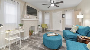A living room with a blue sofa, a round ottoman, a white desk, and a fireplace. - Centrally Located Near Downtown W/ In Unit W&D! (Wichita)