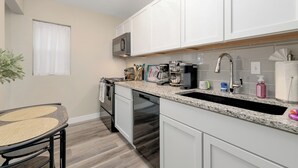 A kitchen with white cabinets, a granite countertop, stainless steel appliances, and a window with white curtains. - Centrally Located Near Downtown W/ In Unit W&D! (Wichita)